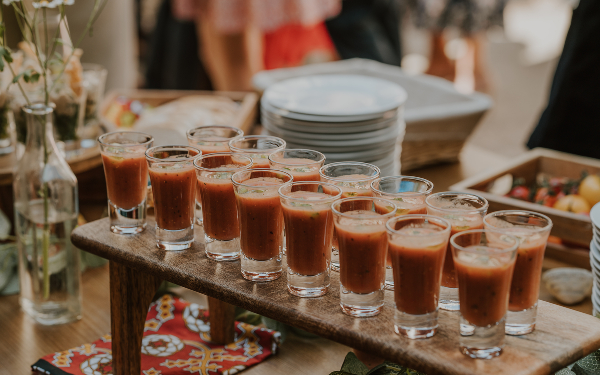 Row of gazpacho shot glasses lined up on a wooden stand at the canape station
