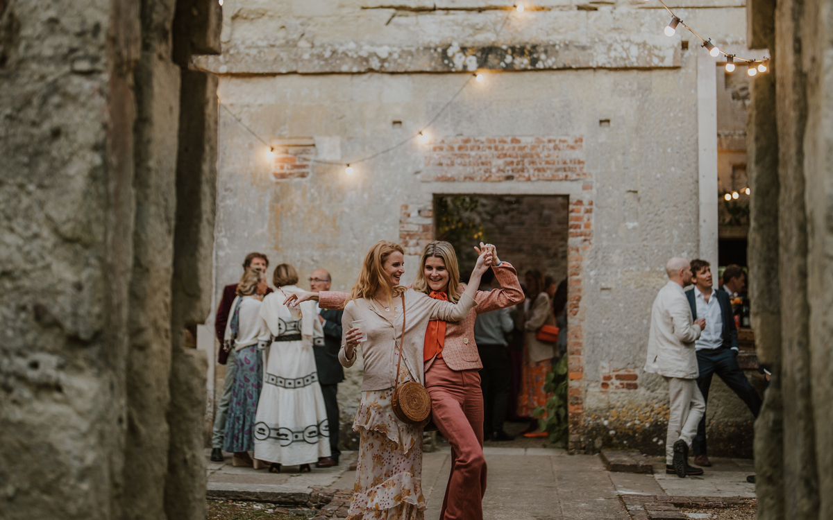 Two friends dancing and laughing inside the candlelit walled ruins during the reception