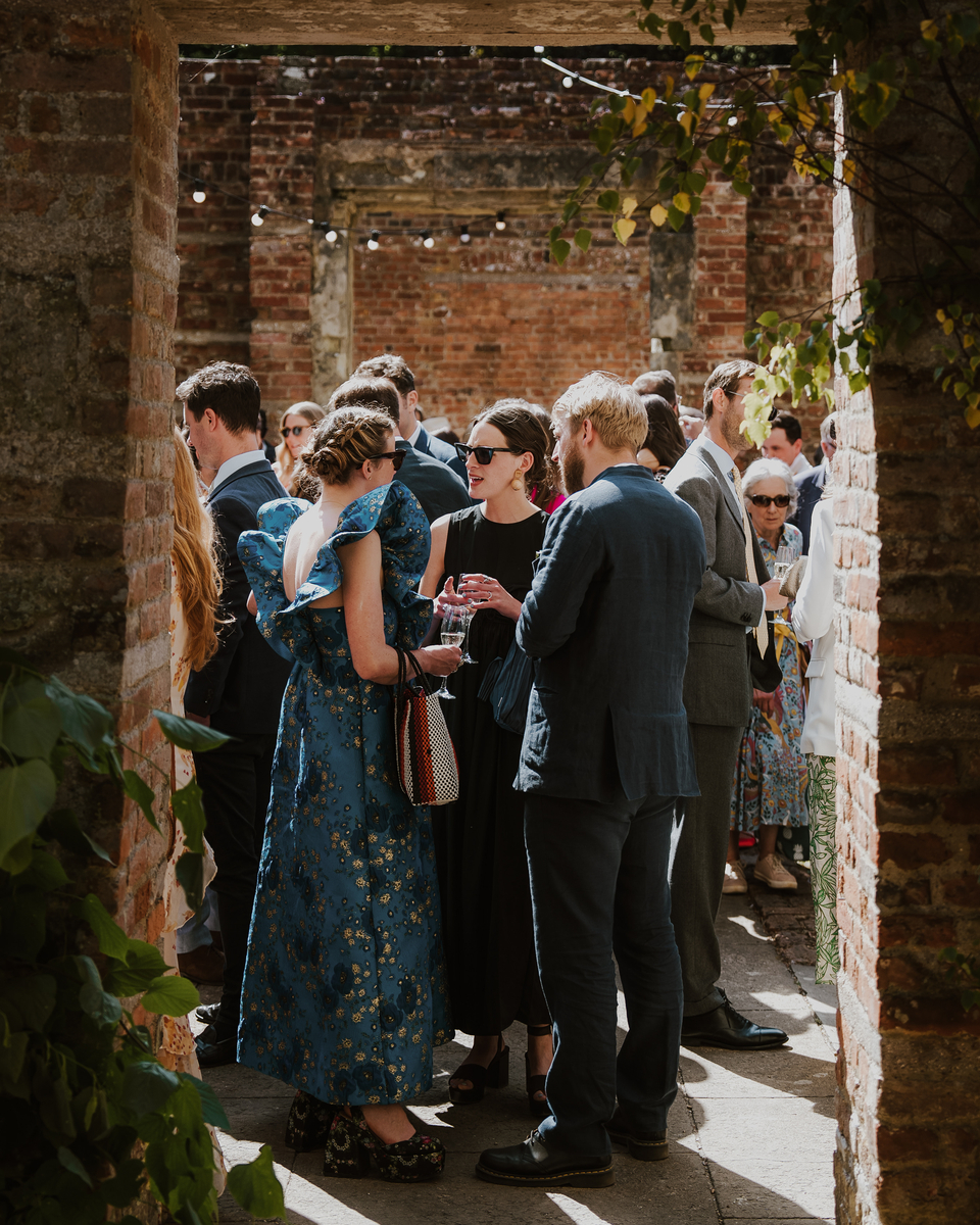 Guests in floral and linen attire chatting through a brick archway in the walled garden