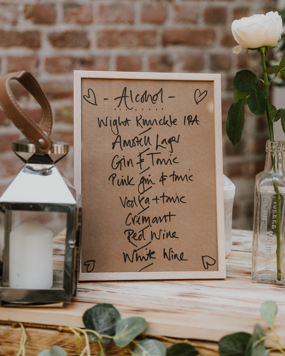 Handwritten drinks menu on kraft paper beside a single white rose and a lantern