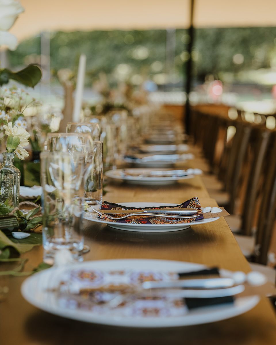 Long wooden banquet table with paisley napkins, gold cutlery and white florals down its centre