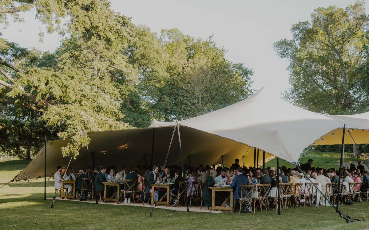 Wide view of a sailcloth tent reception filled with guests on the lawn at Appuldurcombe House