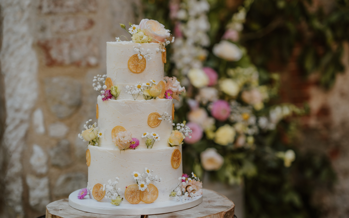 Three tier white wedding cake decorated with dried citrus slices and pastel wildflowers