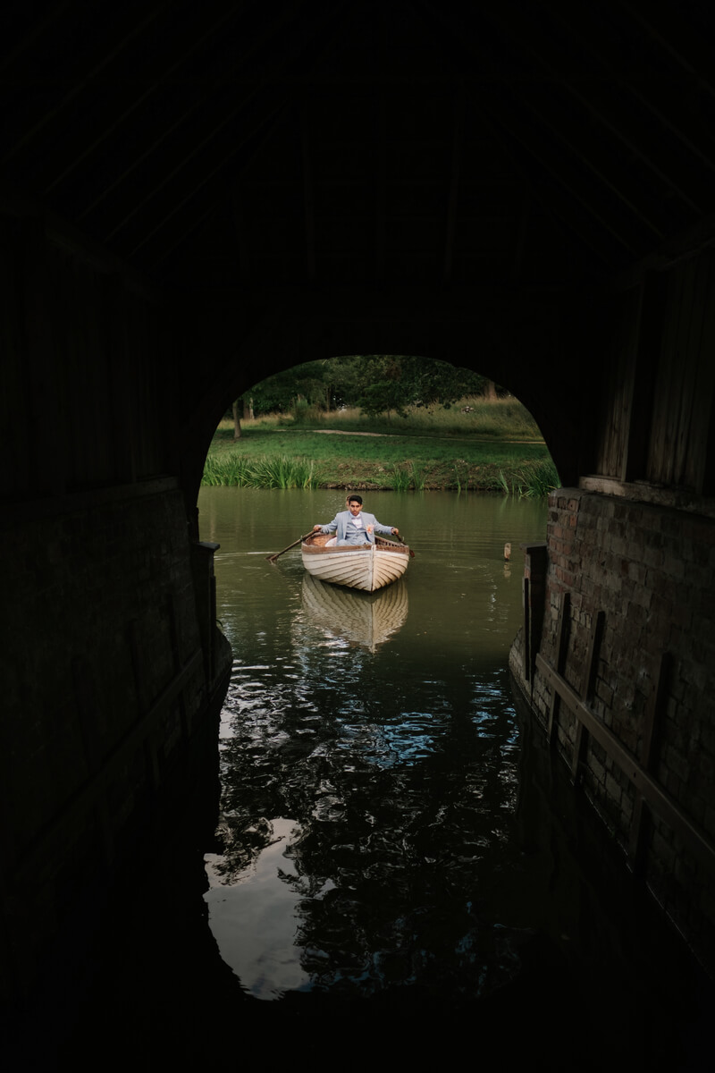 Lily & Ash drifting beneath the boathouse arch in a wooden boat
