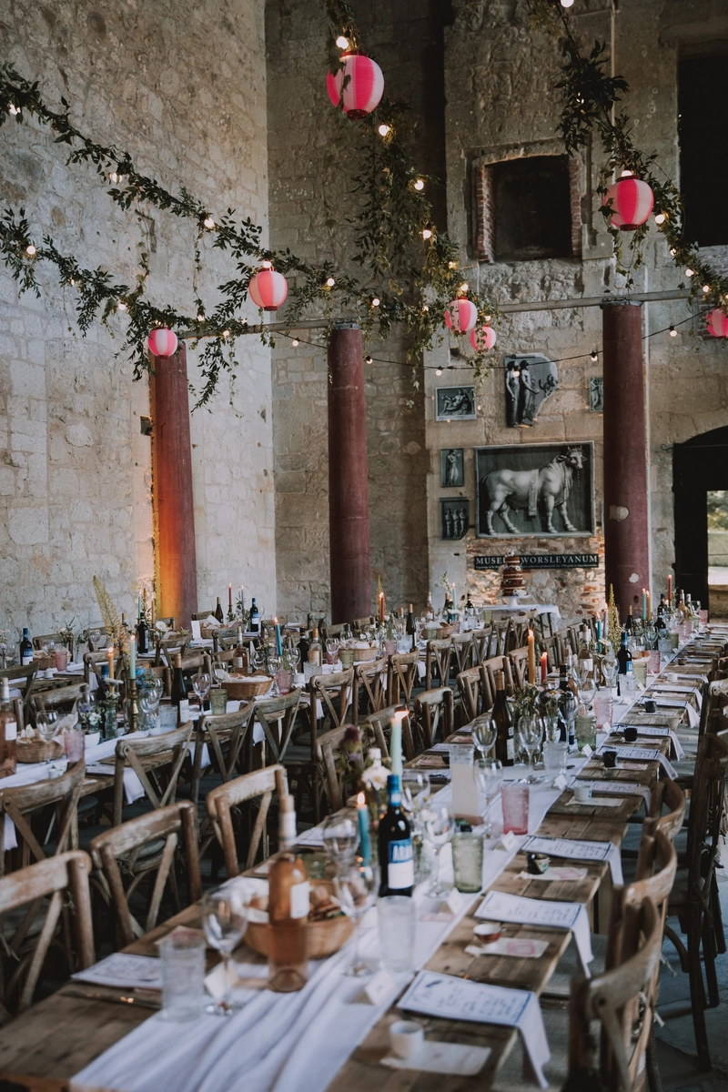 Long candlelit reception tables inside the ruin, strung with lanterns beneath a mounted stone bull and framed portraits