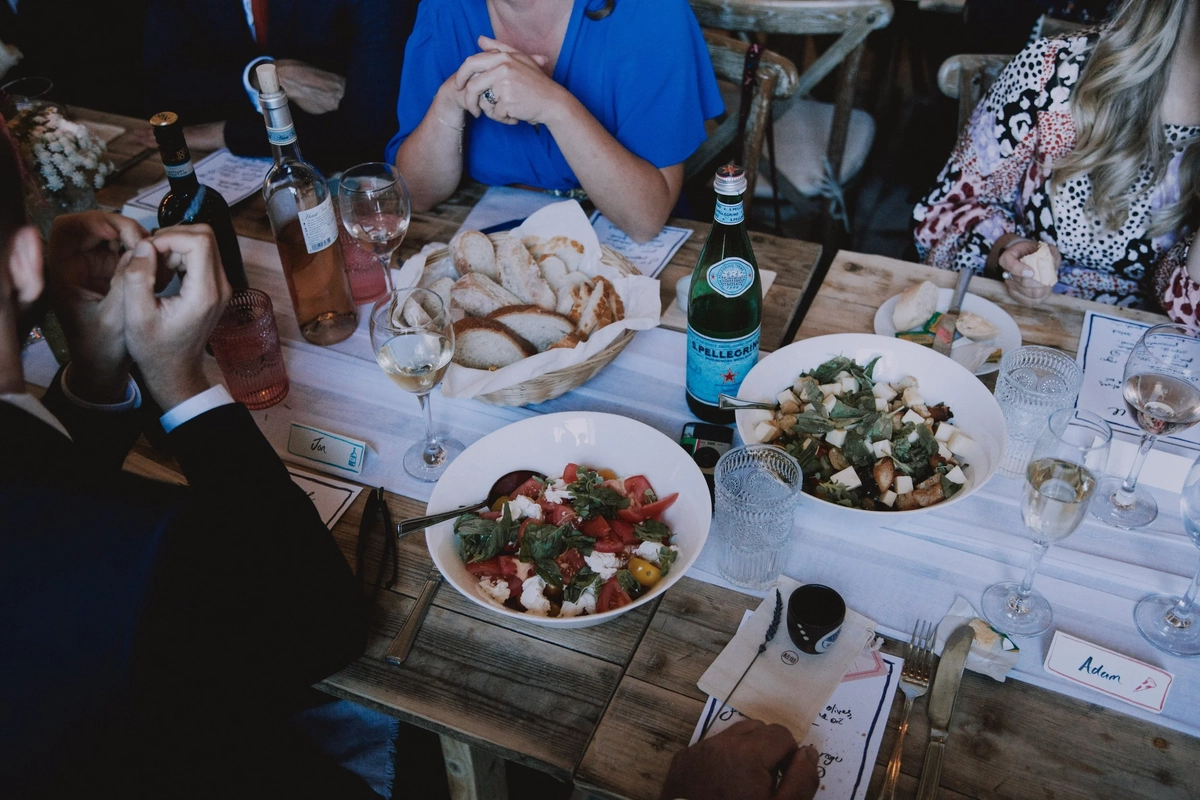 Guests share bread, caprese salad and glasses of rose at a long trestle table set with hand-lettered place cards