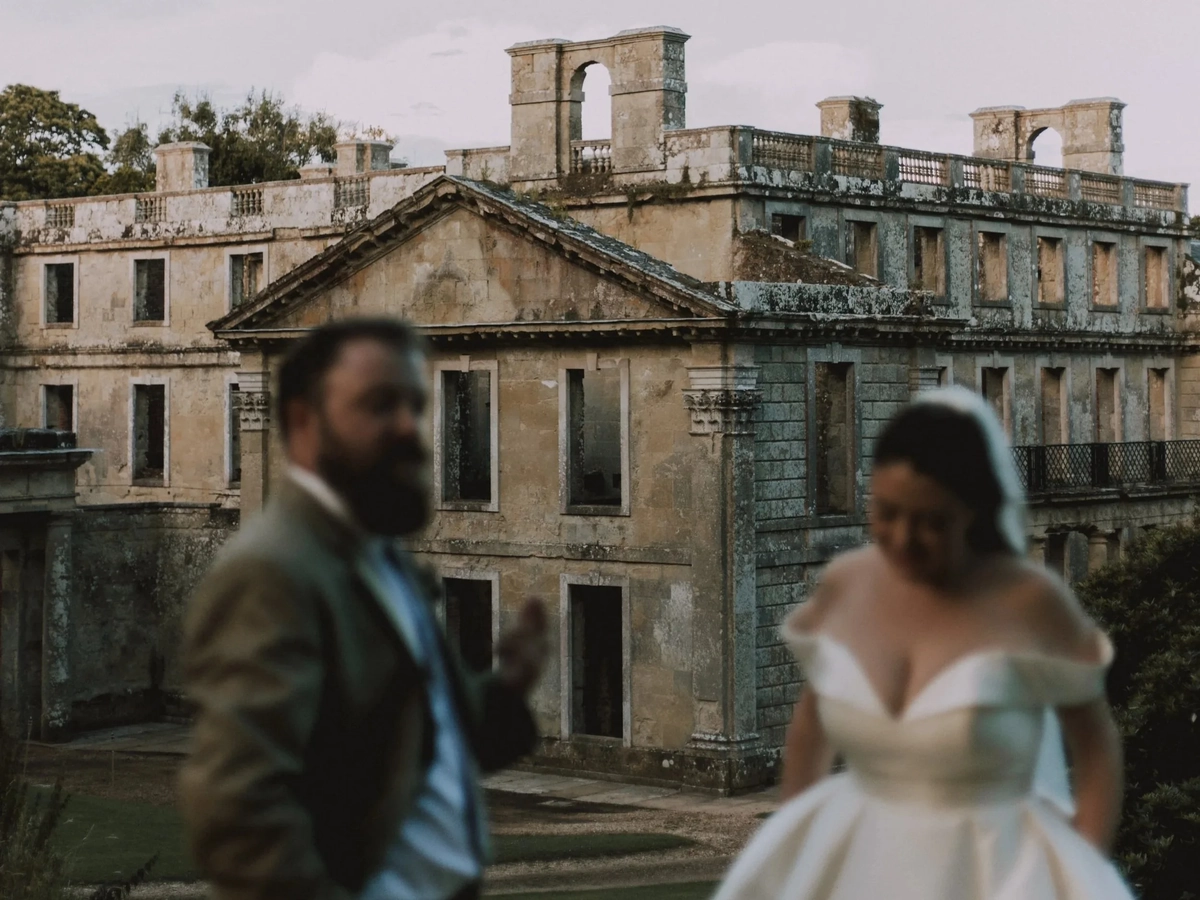 Soft-focus portrait of the couple walking with the ruined facade of Appuldurcombe House rising sharp behind them