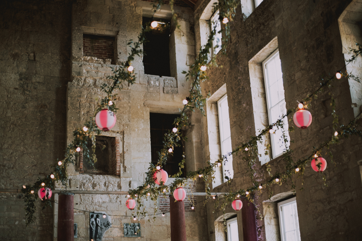 Strings of fairy lights and pink paper lanterns wound with ivy hang between the tall stone columns of the reception ruins
