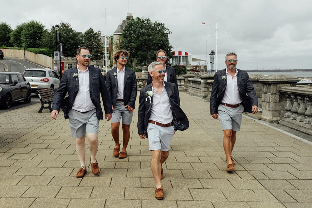 Adam and his groomsmen striding along the Cowes seafront in matching tweed jackets, grey shorts and boat shoes