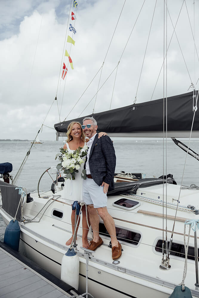 Rosie & Adam laughing on the deck of a moored sailing yacht strung with nautical signal flags, Royal Ocean Racing Club, Isle of Wight
