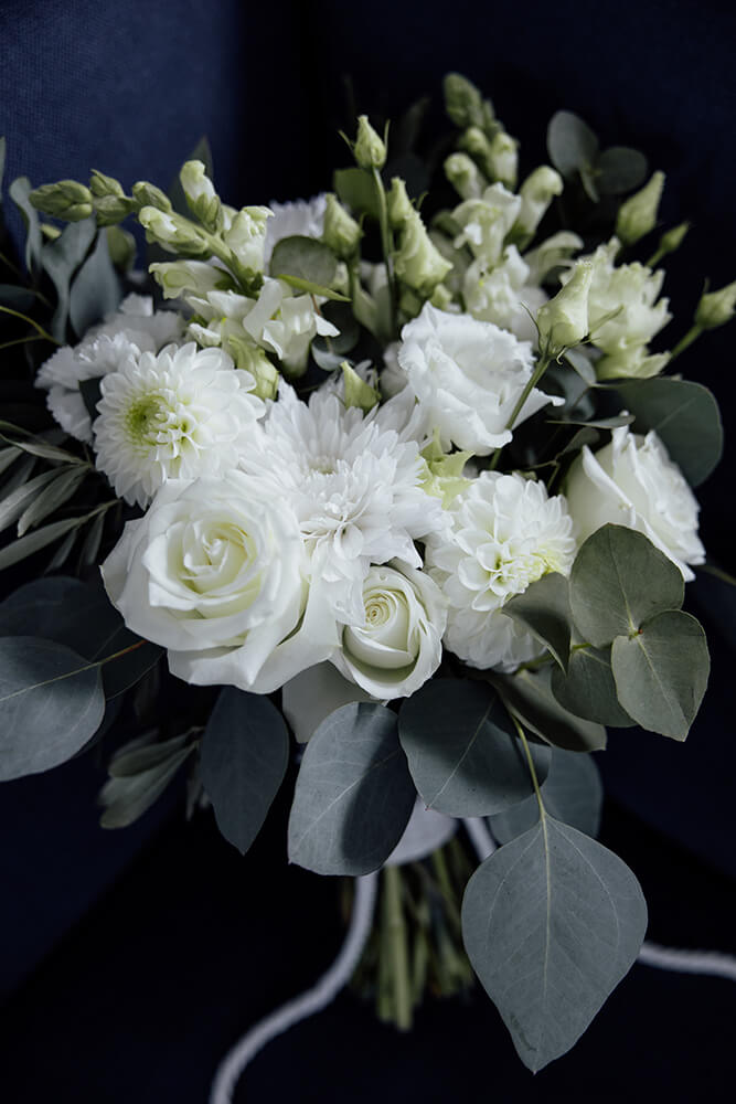 Close-up of the bridal bouquet, white roses, dahlias and snapdragons mixed with trailing eucalyptus against a navy backdrop