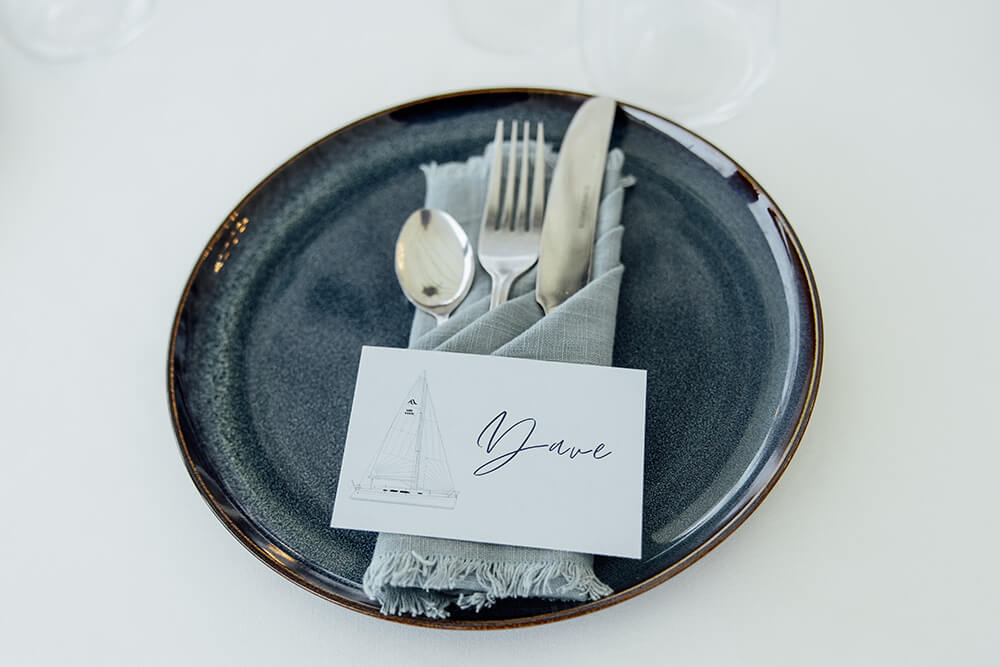Place setting with a hand-illustrated sailing boat name card reading "Dave", slate plate and linen napkin on the reception table