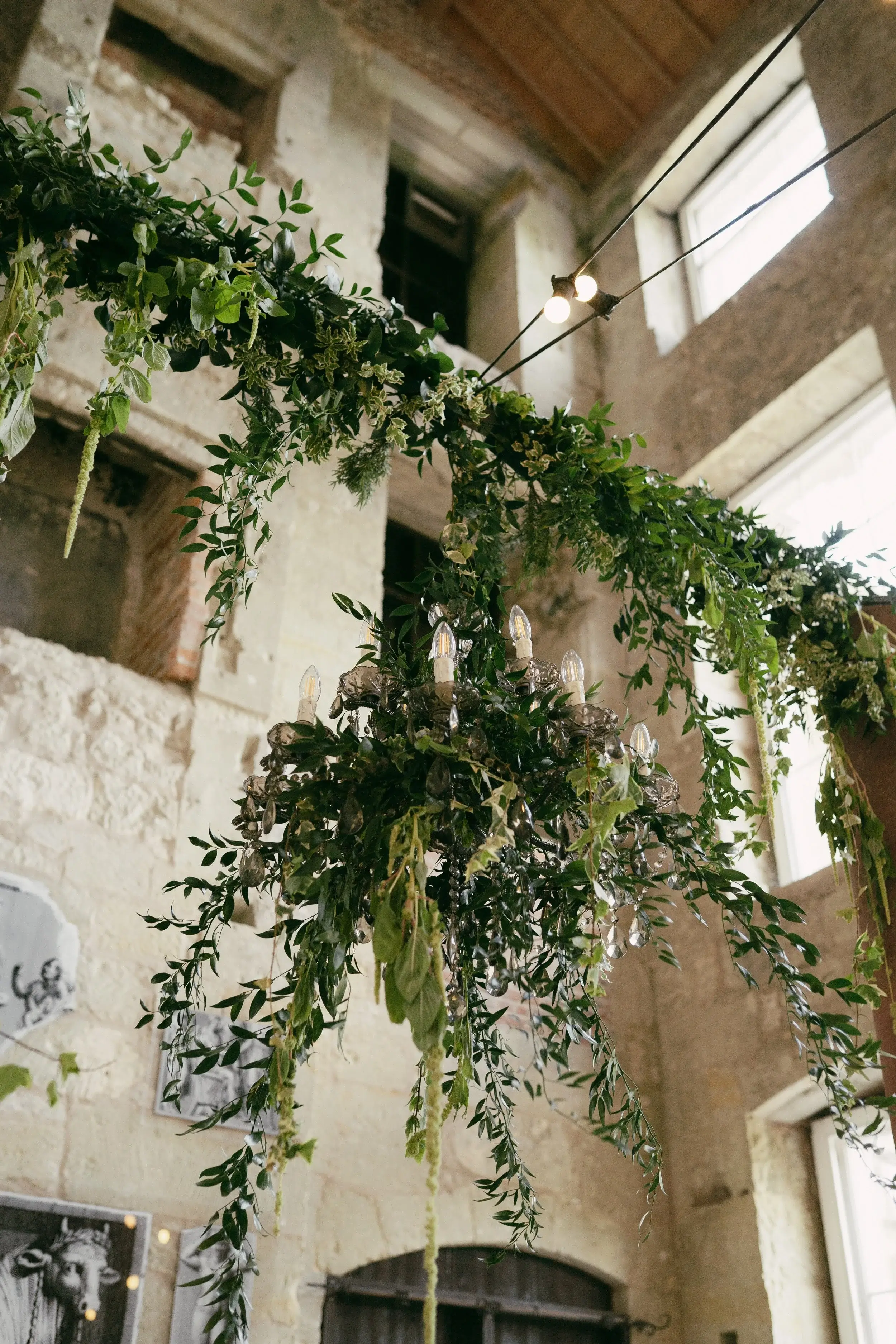 Chandelier dressed with trailing ivy and crystal drops hanging from the ruined stonework above the reception tables