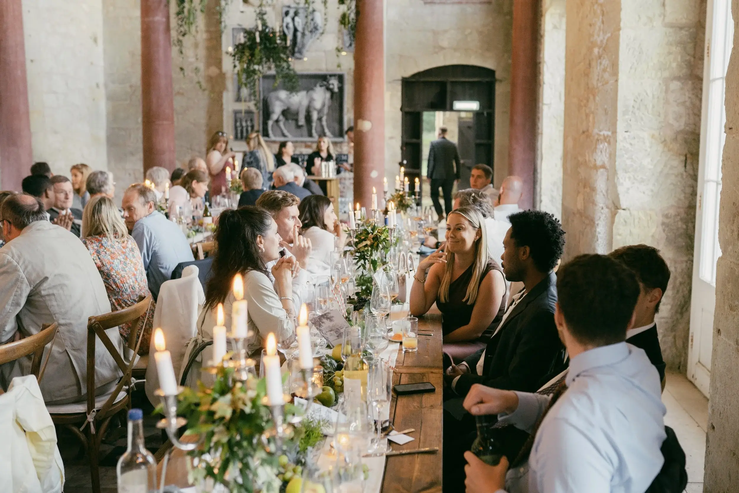 Guests seated at the long candlelit table laughing and chatting during the wedding breakfast in the Great Hall