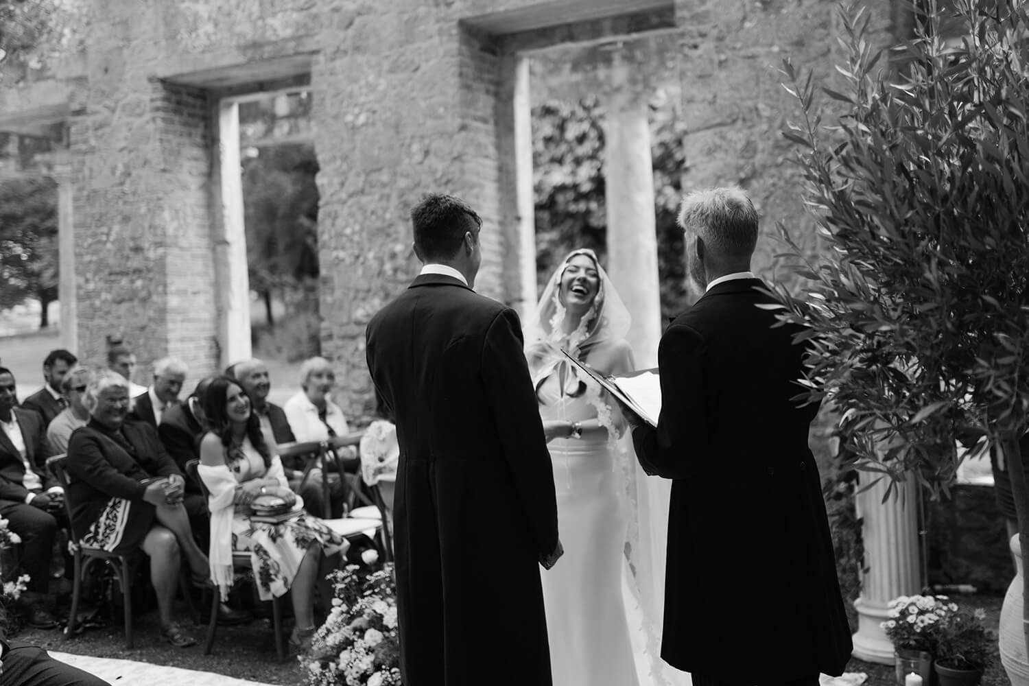 Black and white moment of the bride laughing during her vows as the groom and celebrant stand facing her at Appuldurcombe House