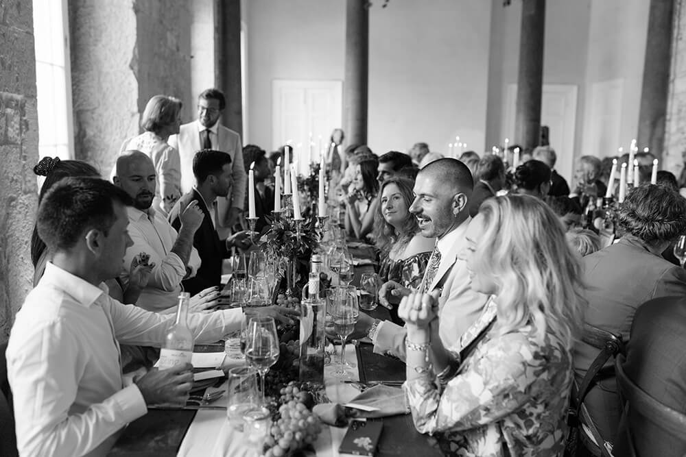 Black and white candid of wedding guests laughing together at the long table during the reception