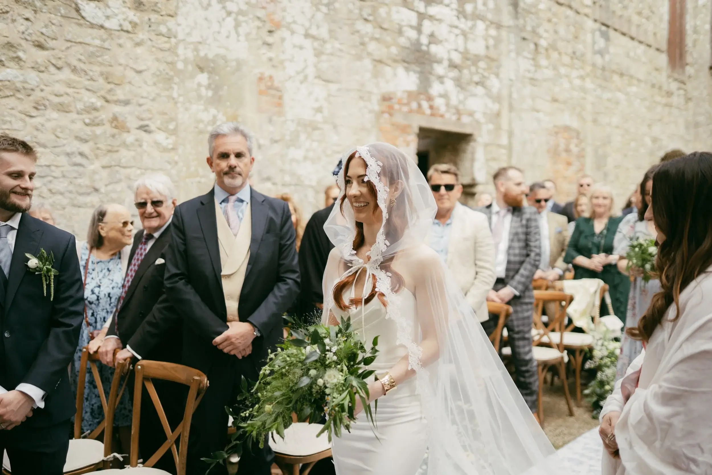 Long feasting table set beneath festoon lights and hanging greenery, flowers cascading from the bench in the roofless Great Hall