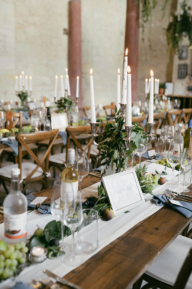 Table setting named Neptune with lit taper candles, trailing ivy, grapes and figs, and a denim blue napkin