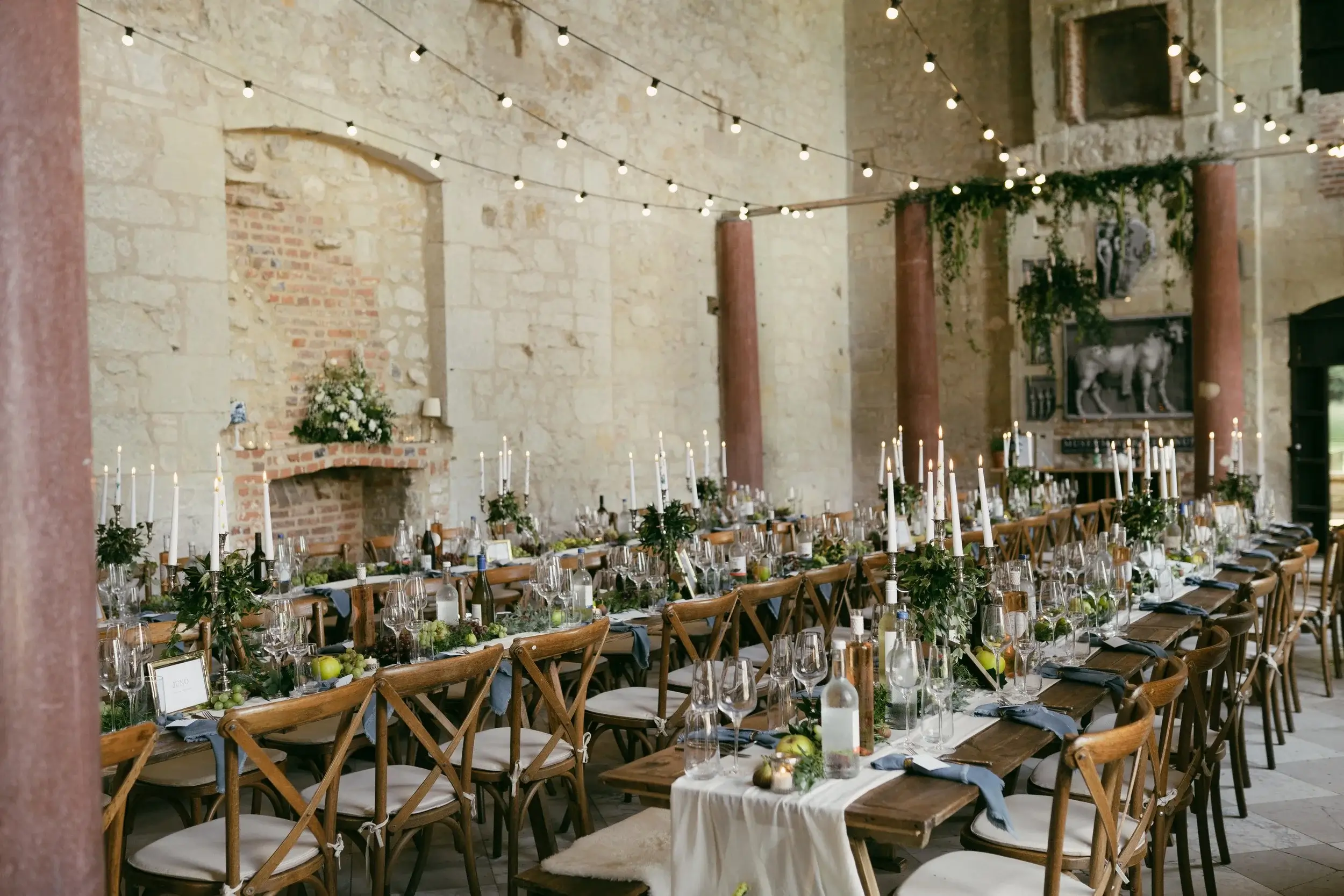 Long banqueting tables laid with candelabras and greenery inside the roofless Great Hall, festoon lights strung high overhead