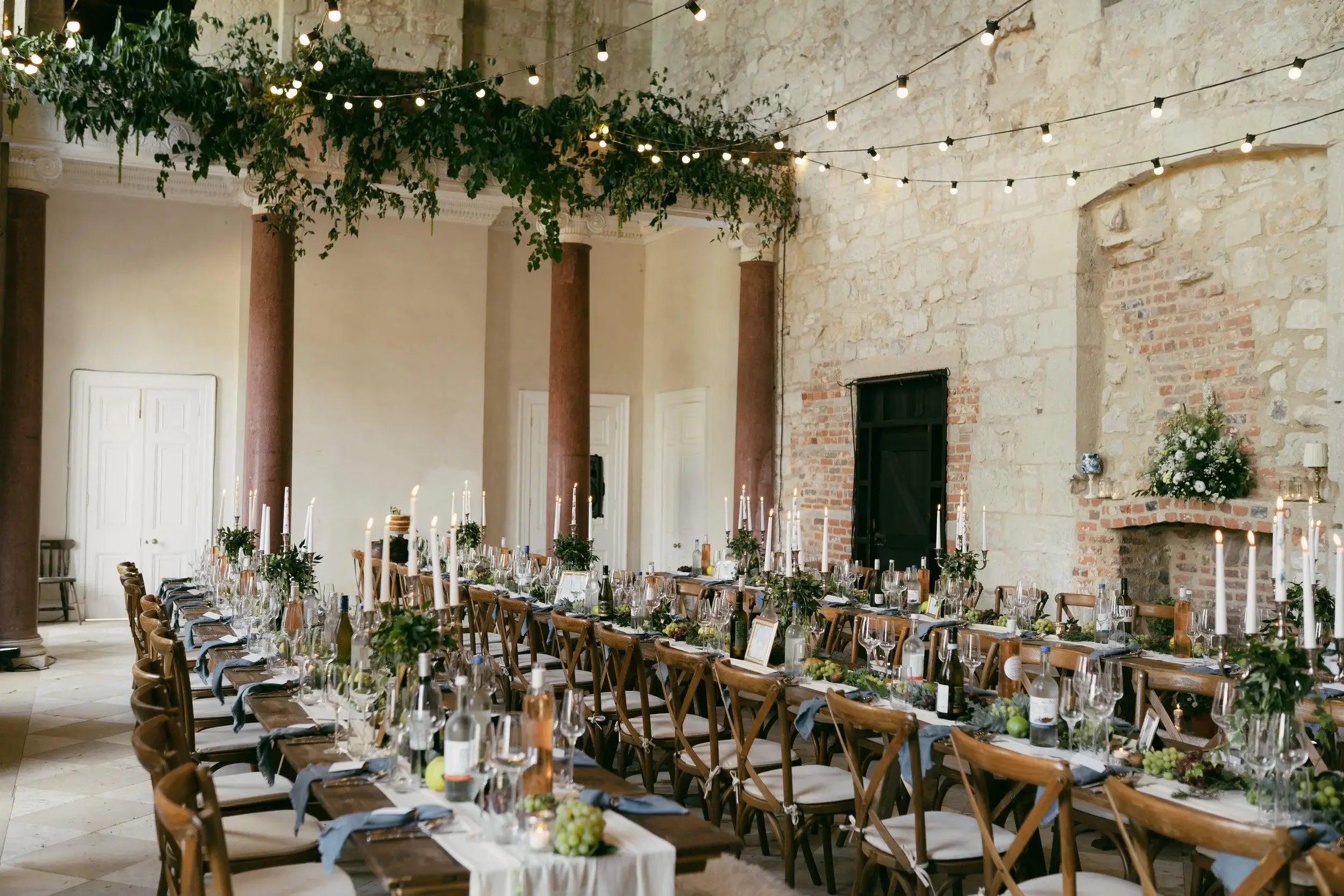 Wide view of the Great Hall reception tables lined with candles beneath a garland of greenery and festoon lights